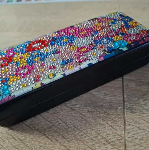 Colorful rhinestone-studded pencil case with rainbow sequin design in black holder on wooden surface