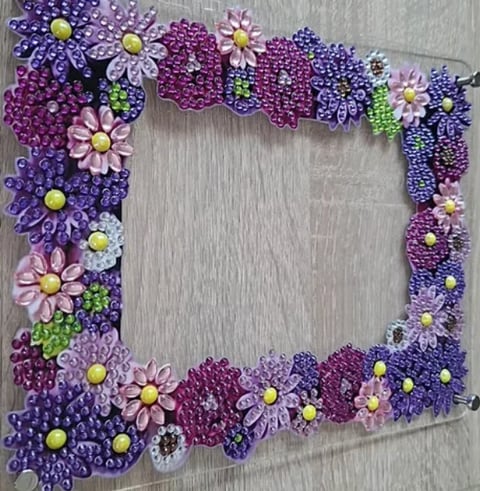 Decorative beaded flower frame border in purple, pink, and green tones with open center on gray wooden surface