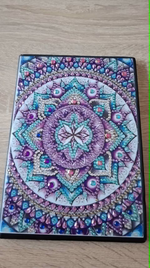 Ornate diamond-shaped mandala design with purple, turquoise, and pink jeweled embellishments on a black background
