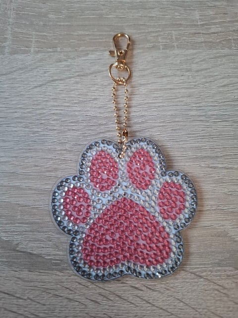 Red and white paw print keychain with rhinestone embellishments and gold chain clip on wooden background