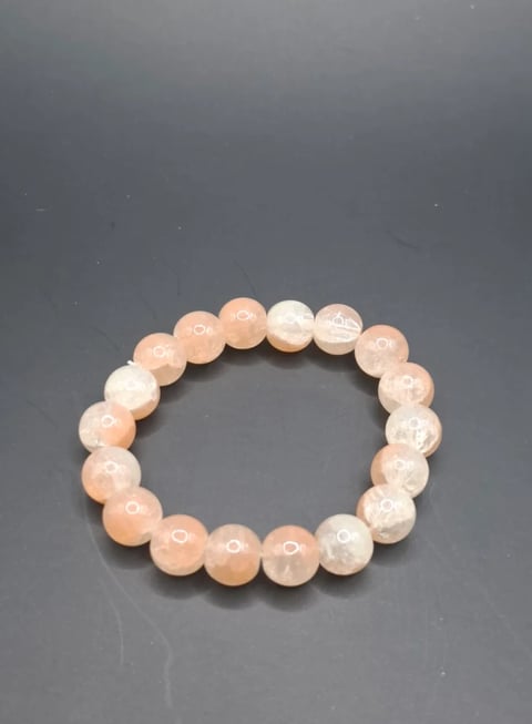 Beaded bracelet with smooth round stones in peach and white tones on gray background