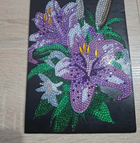 Rhinestone artwork of purple and white flowers with yellow centers and green leaves on black canvas