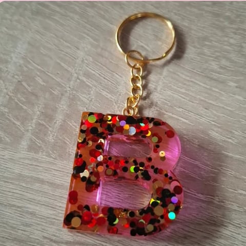 Pink sequined letter B keychain with gold ring and chain on wooden background