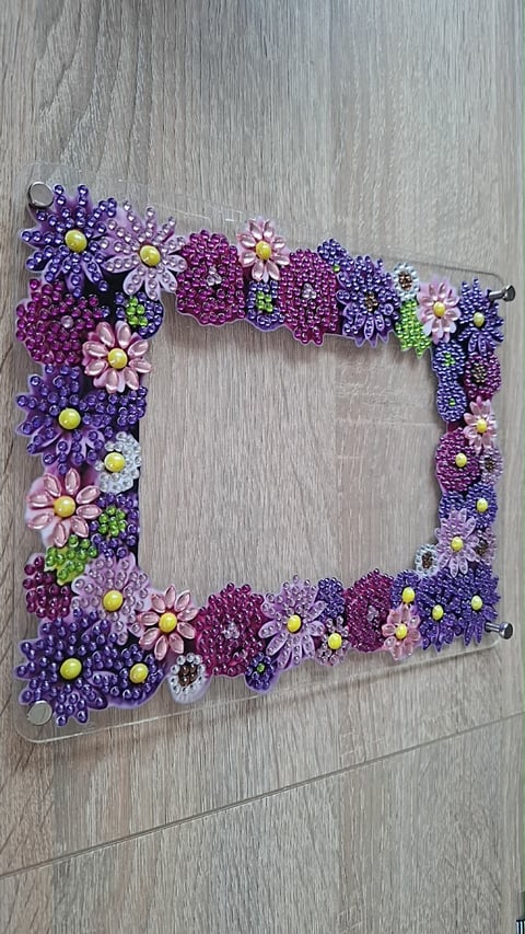 Beaded picture frame with purple, pink, and green flowers on wood background