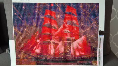 Pixel art or cross-stitch image of a red sailing ship with full sails against a purple twilight sky with stars