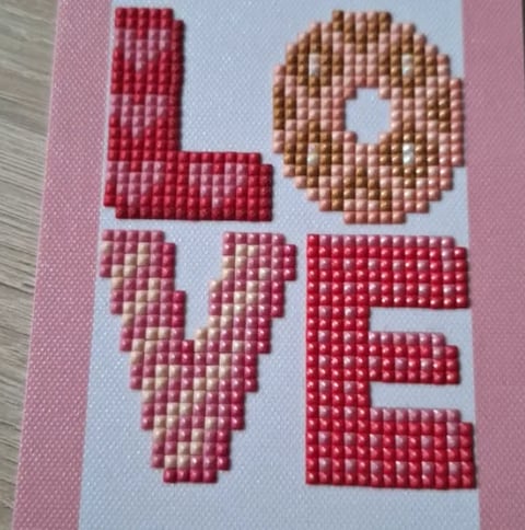 Cross-stitch LOVE artwork with red and brown beaded letters on white canvas with pink border