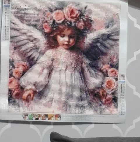 Vintage-style cross-stitch pattern showing an angel with pink roses, white dress, and gray wings on printed fabric
