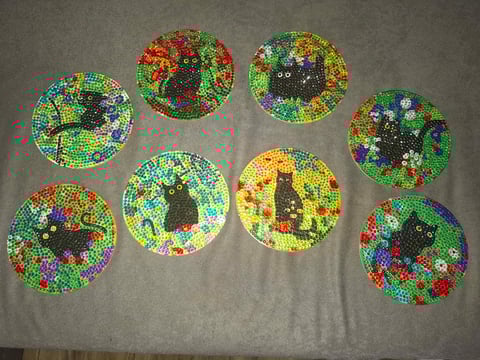 Eight colorful beaded circular patterns with black centers arranged on a gray fabric background