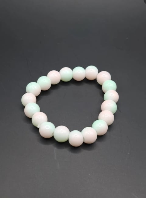 Beaded bracelet with alternating pale pink and light green spherical beads arranged in a circular pattern on gray background
