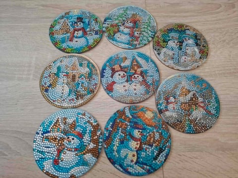 Eight decorative coasters with beaded snowman designs in turquoise, red, and white on a wooden surface