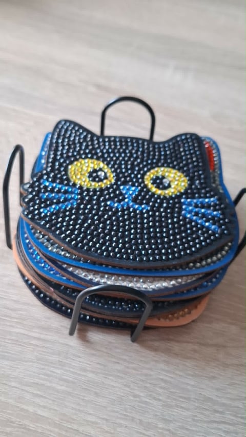 Decorative cat-shaped beaded coin purse with yellow eyes, blue stripes, and metal handle on wooden surface