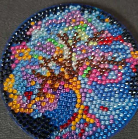 Colorful beaded circular design featuring a tree with brown trunk and multicolored beads in blue, pink, yellow, green, and red tones