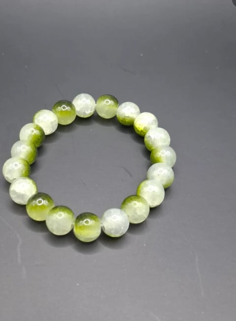 Beaded bracelet with alternating white and yellow-green spherical beads arranged in a circle on gray background