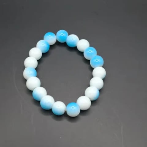 Beaded bracelet made of alternating light blue and white spherical beads arranged in a circular pattern on gray background