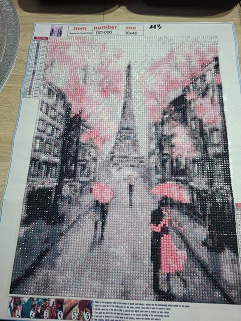 Diamond painting canvas showing a street scene with pink umbrellas, buildings, and a church spire in the background