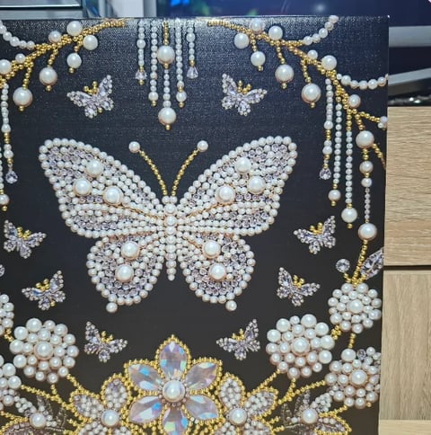 Decorative dark canvas with pearl-embellished butterfly and floral designs in white, gold, and iridescent beads