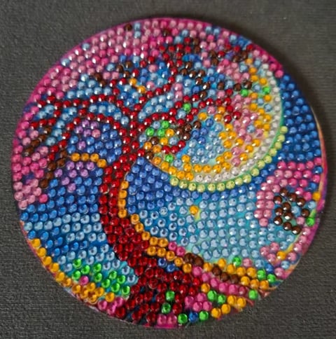 Colorful circular rhinestone craft featuring a swirling galaxy or nebula design with pink, blue, red, yellow, and green sequins on a dark background