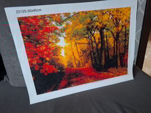 Diamond painting artwork showing a sunset forest scene with golden trees, red sky, and warm autumn colors on white paper