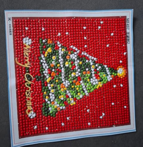 Beaded Christmas tree decoration on red background with white snow beads and gold text reading Merry Christmas