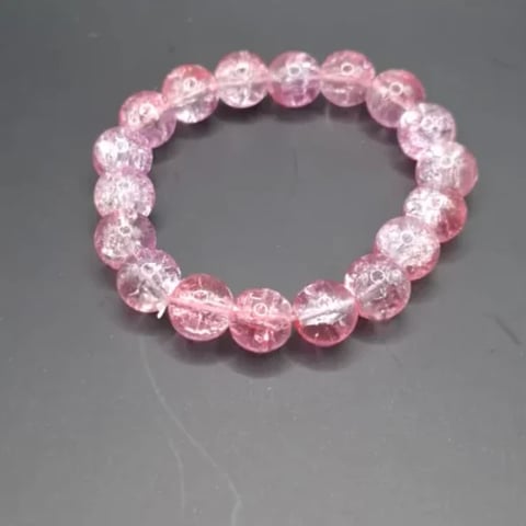 Pink beaded bracelet with clear crackle and sparkle beads arranged in a circular pattern on gray background
