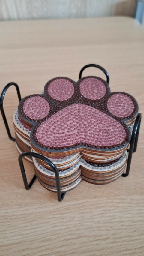 Paw print-shaped coaster set with pink textured top and striped cork backing in black metal holder on wooden table