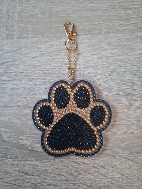 Paw print keychain with black and gold rhinestone embellishments and gold chain attached to clasp