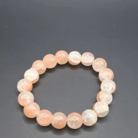 Beaded bracelet made of translucent peach and white round stone beads arranged in a circle on gray background