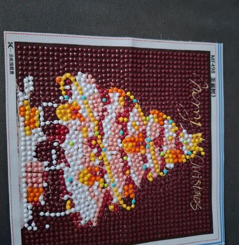 Beaded maple leaf craft on burgundy background with white, yellow, orange, and red beads forming an autumn leaf design with script text