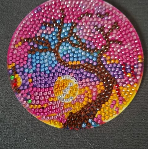 Circular rhinestone craft featuring a colorful iguana head design with blue, yellow, pink, and brown gems on a pink background