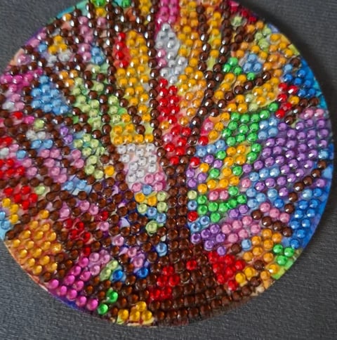 Circular beaded craft with radiating sections of multicolored rhinestones in rainbow pattern
