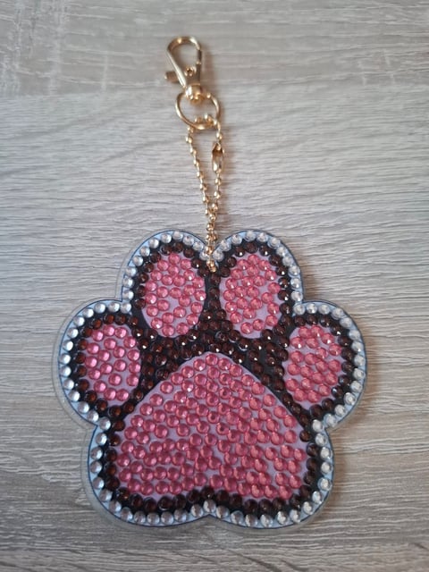 Sparkly pink paw print keychain with rhinestone border on wooden surface