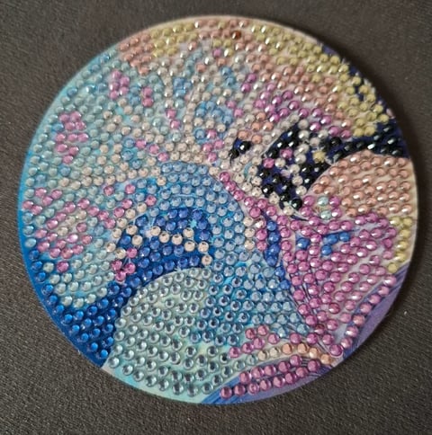 Round rhinestone art featuring a colorful parrot head with blue, pink, purple, and yellow gems on gray background