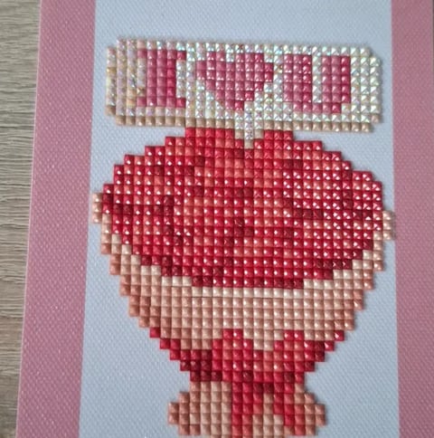 Pixel art beadwork of a strawberry with leaves on pink background, handmade craft project