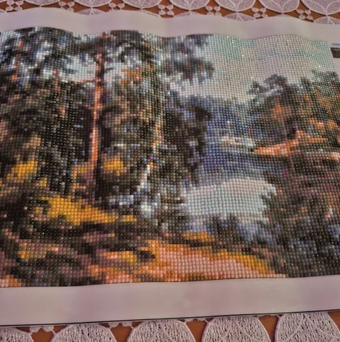 Pixel art cross-stitch or beadwork depicting a forest landscape with tall trees and warm sunset tones in orange and yellow