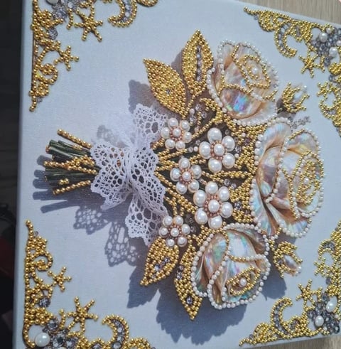 Ornate beaded embroidery featuring a golden flower with white lace center and pearl accents on a light background