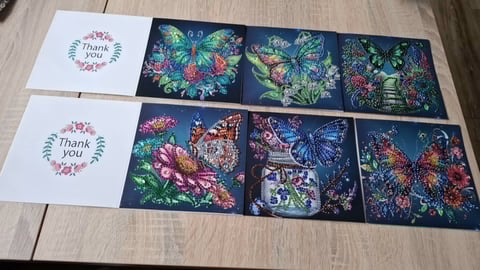 Arrangement of thank you cards with pink floral wreaths and dark floral patterned cards with colorful flowers displayed on wood surface