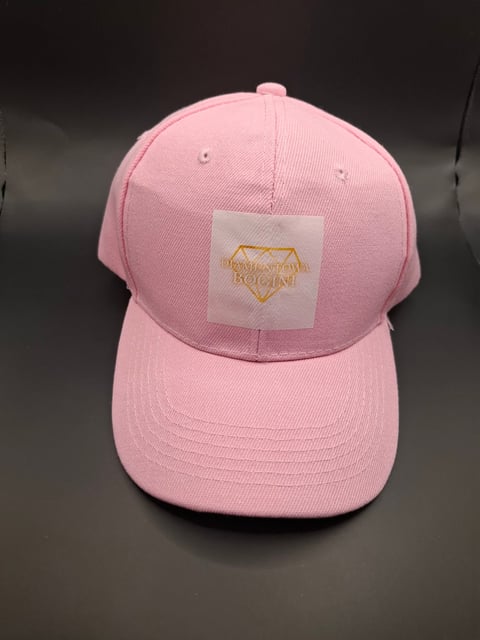 Pink baseball cap with white patch featuring gold geometric logo on dark background