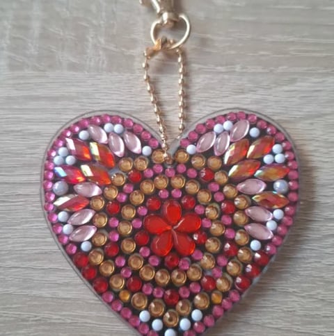 Decorative heart pendant with colorful rhinestones and beads arranged in a floral pattern, hanging from a chain