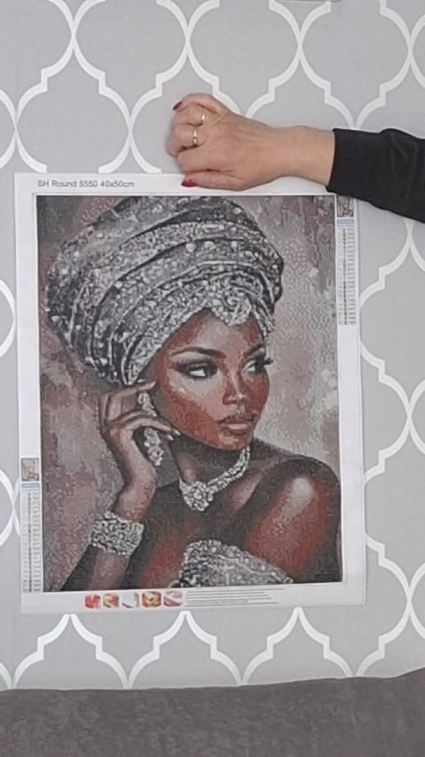 Persons hand holding a printed portrait of a woman wearing ornate gold jewelry and a wrapped head covering against a patterned wall