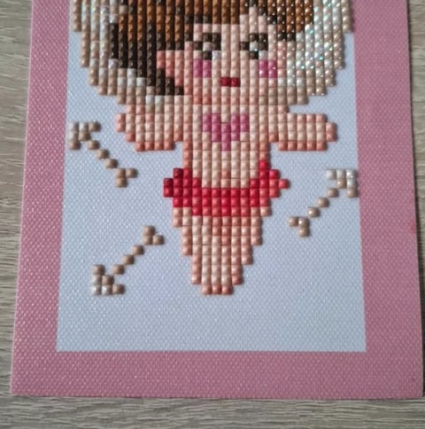 Cross-stitch pixelated portrait of a girl with brown hair and pink dress on light blue background with pink border