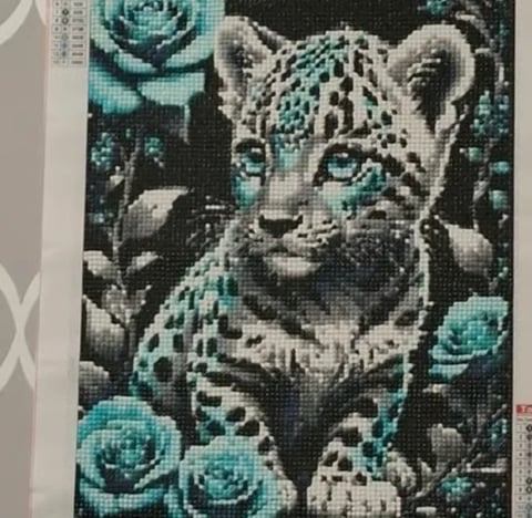 Cross stitch pattern of a spotted leopard cub surrounded by turquoise roses on a dark background