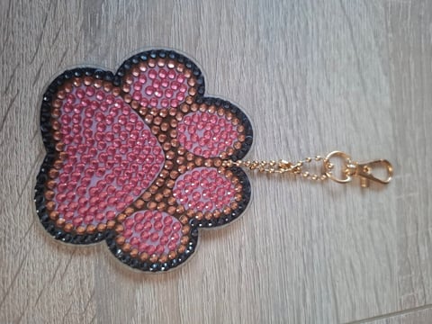 Pink rhinestone flower-shaped keychain with gold clasp on wooden surface