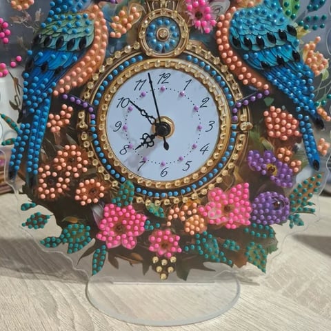 Ornate decorative clock with beaded floral design in pink, purple, and blue beads surrounding a white clock face with gold trim