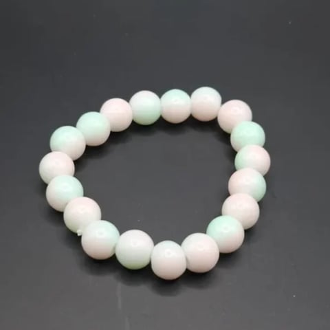 Beaded bracelet with alternating pale pink and mint green spheres on elastic band against gray background