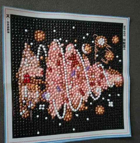 Diamond painting craft showing a pink and white floral design with beads on a black pegboard canvas