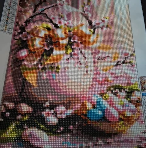 Partial diamond painting with pink blossoms, orange butterflies, and black branches on a grid canvas