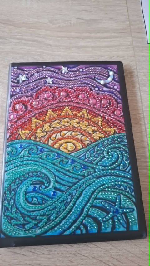 Colorful beaded artwork on black canvas featuring layered landscape design with night sky, sunset, and ocean waves in purple, pink, yellow, and turquoise