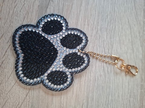 Black and silver rhinestone paw print keychain with gold chain and clasp on wooden surface