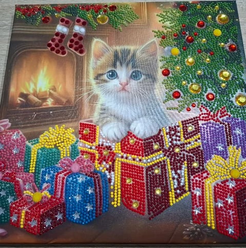 Diamond painting of a white kitten surrounded by festive Christmas decorations, gifts, and a fireplace with holiday garland