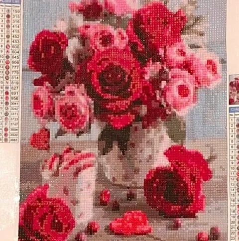 Diamond painting of pink and red roses arranged in a white vase with green leaves and loose petals